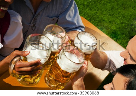 Group of four people in Couple in traditional Bavarian dress, Lederhosen and Dirndl, in a beer garden or at a festival like the Oktoberfest; focus on beer steins