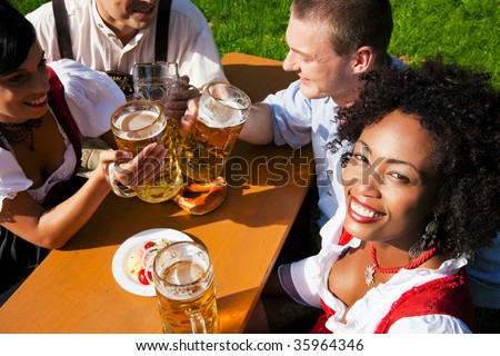 Group of four people in Couple in traditional Bavarian dress, Lederhosen and Dirndl, in a beer garden with Pretzel and Obatzter (traditional cheese)