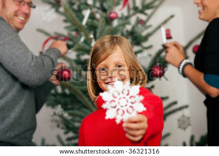 Young girl helping her family decorating the Christmas tree, holding a Christmas Snowflake in her hand