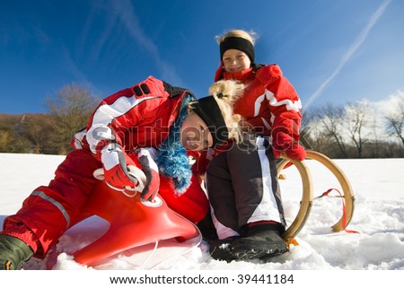 Two little children with their toboggan at the top of a hill in the snow waiting to start the fun