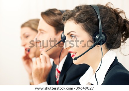 Group of three customer care representatives in a call center with headphones