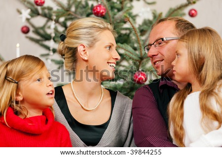 Family sitting on Christmas day in front of the Christmas tree, smiling