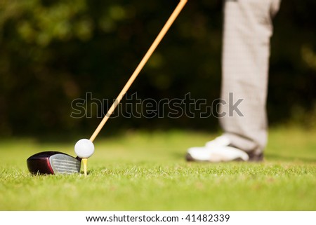 Golf player attempting the first stroke in the teeing area (only legs of player to be seen, focus on ball)