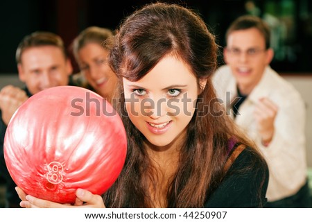 Group of four friends in a bowling alley having fun, three of them cheering the one in charge to throw the ball