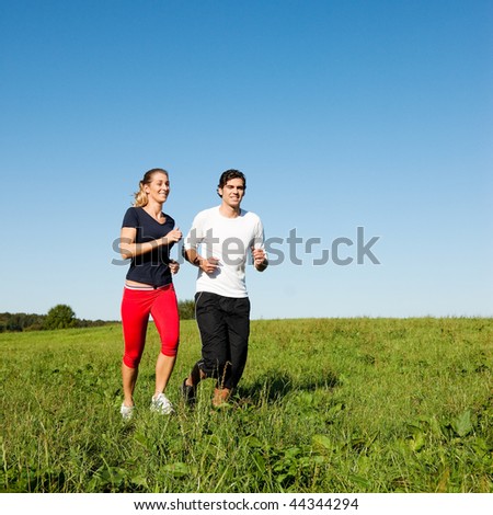 Young fitness couple doing sport outdoors, jogging on a green summer meadow in the grass under a clear blue sky