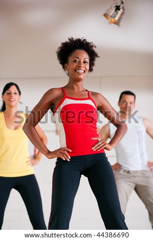 Group of three people in colorful cloths in a gym doing step gymnastics, a female instructor in front