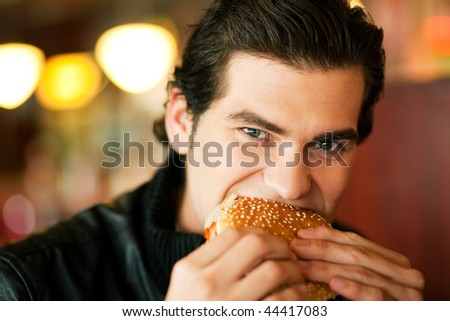 Man in a restaurant or diner eating a hamburger, he is hungry and having a good bite, shot with available light, very selective focus