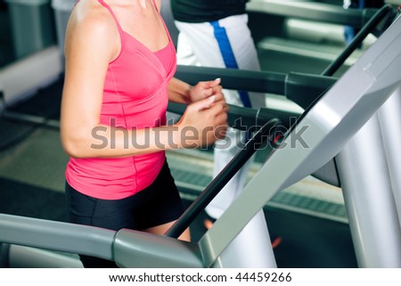Woman and man in gym - only legs to be seen - exercising running on the treadmill to gain more fitness; motion blur in limbs for dynamic