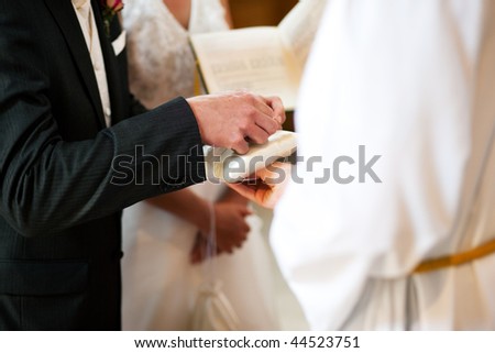 Couple having their wedding ceremony in church in front of a catholic priest, groom taking the ring to give it to the bride