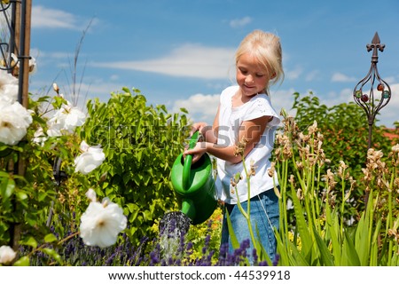 Little girl watering the flowers in the family garden at a summer day, very rural scene