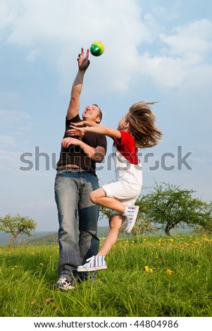 Father and daughter playing with a football, the kid trying to catch it running and jumping
