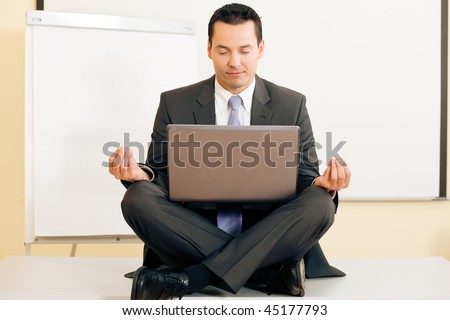 Office worker - a male manager - meditating cross legged upon his table, being very relaxed, a metaphor for work life balance