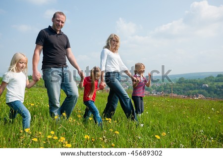 Happy family with Children walking down a meadow with dandelion flowers at a bright spring day, in the background a village is to be seen