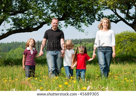 Happy family with Children walking down a meadow with dandelion flowers at a bright spring day