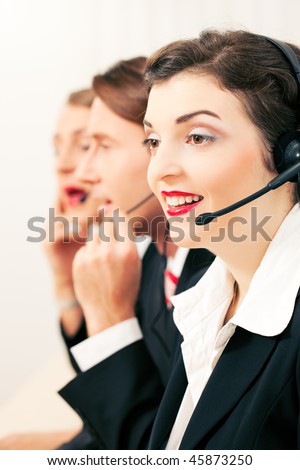 Group of three customer care representatives in a call center with headphones rendering service to callers