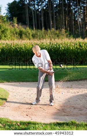 Mature or senior couple playing his ball out of a sand trap, ball in motion and lots of sand frozen (short shutter speed)