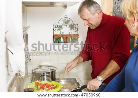 Senior or best ager couple cooking dinner together in their home kitchen, doing salad and preparing minced meat in a pan