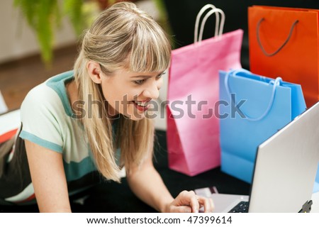 Woman lying in her home living room on floor shopping or doing banking transactions online in the Internet, emphasized by shopping bags in the background