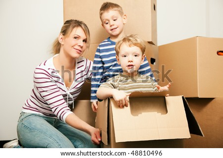 Family moving in their new house. The sons are sitting inside the moving boxes, everybody is looking rather cheerful