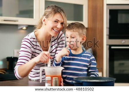 Family cooking in their kitchen - mother making some spaghetti sauce, son having a taste licking his finger for it