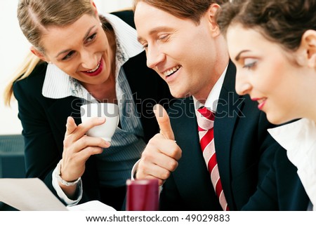 Small business team - man and two women - working in the office having a success, one woman drinking a mug of coffee