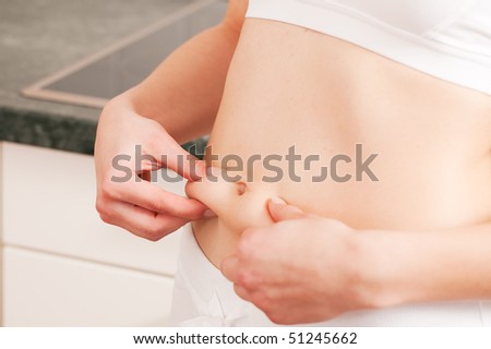 Woman is pinching her love handles being not too satisfied with their status after a long winter - she will have to loose some weight