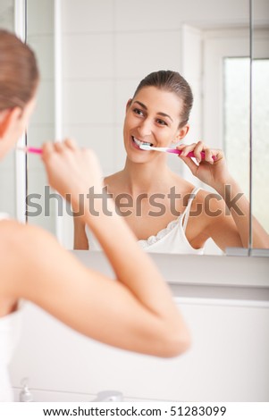 Young woman with light brown hair brushing her teeth after happily waking up in the morning