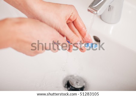 Young woman, just her hands are to be seen, is washing her toothbrush at the basin after she brushed her teeth in the morning