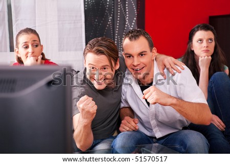 Two couples watching sports in the telly, the guys are really excited and cheer their team while the girls are quite bored
