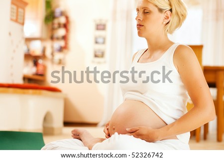 Pregnant woman doing pregnancy yoga sitting on the floor in her home