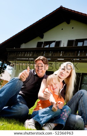 Young family sitting in the sun on the lawn in front of their new home - a single house