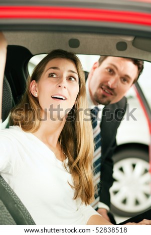 Woman buying a car in dealership sitting in her new auto, the salesman talking to her in the background