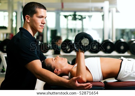 Woman with her personal fitness trainer in the gym exercising with dumbbells