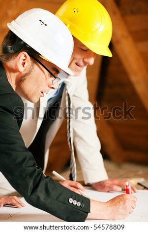 Architect and construction engineer or surveyor discussion plans and blueprints. Both are wearing hardhats and are standing on the construction site of a home indoors