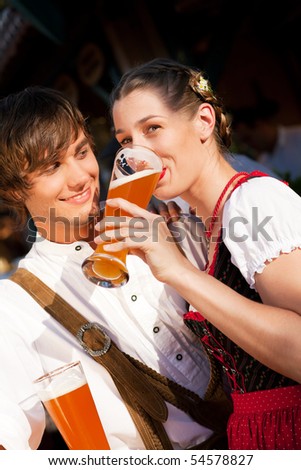 Couple in traditional Bavarian Tracht - Dirndl and Lederhosen - in a beer tent at the Oktoberfest or in a beer garden enjoying a glass of tasty wheat beer