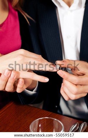 Man gently sticks a diamond ring on the finger of his fiance after a romantic dinner (just hands to be seen)