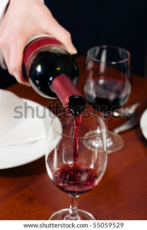 Waitress (just hands to be seen) refills the glass with red wine in a restaurant