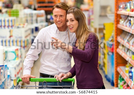 Couple in a supermarket shopping equipped with a shopping cart buying groceries and other stuff, they are looking for what the need