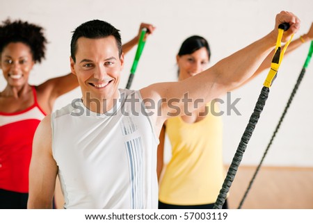 Group of three people in colorful cloths in a gym doing gymnastics with tube equipment