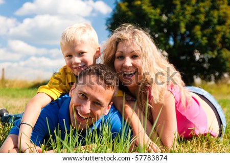 Young family having fun in the sun lying on the meadow an a bright summer day