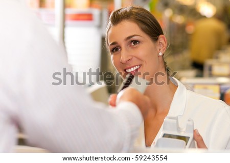 Male customer in supermarket handing his credit card to cashier at the checkout desk in order to pay