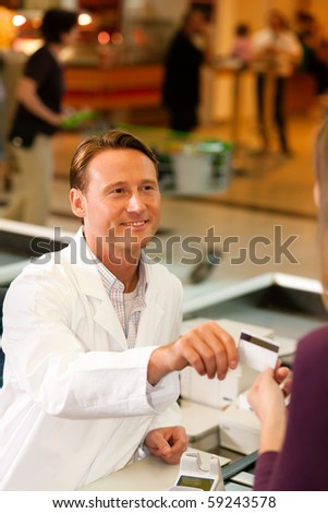 Female customer in supermarket handing her credit card to cashier at the checkout desk in order to pay