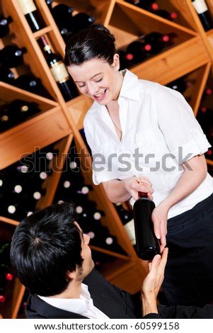 Waitress in a wine bar or restaurant offers a bottle of red wine to a young mediterranean looking man