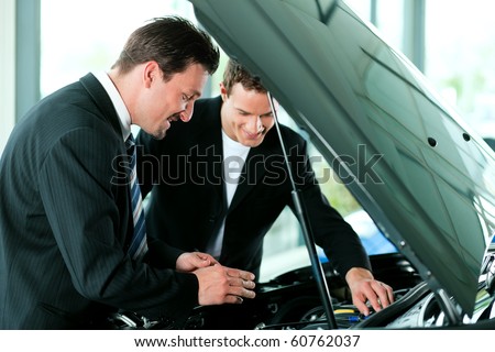 Man buying a car in dealership looking under the hood at the engine