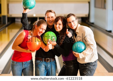 Group of four friends in a bowling alley having fun, holding their bowling balls