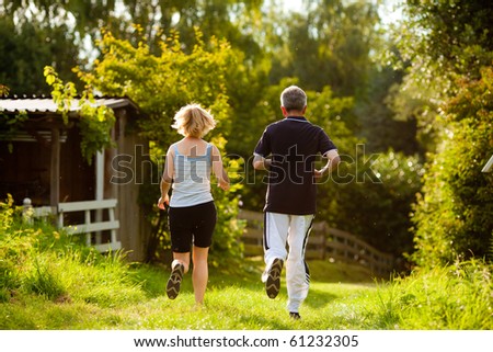 Mature or senior couple doing sport outdoors, jogging down a path in summer, the sun is low on evening