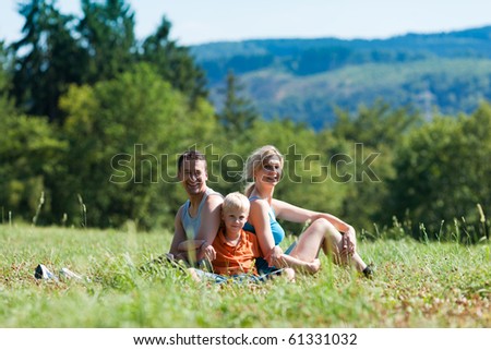 Family in sport clothes sitting on meadow in beautiful landscape, presumably they are resting in between exercises