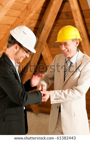 Architect and construction engineer or surveyor shaking hands, Both are wearing hardhats and are standing on the construction site of a home indoors