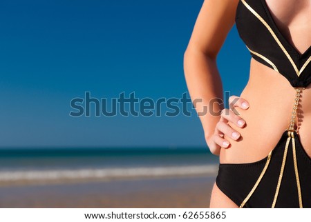 Attractive Woman in monokini standing in the sun on beach, only part of torso to be seen, a lot of copyspace in the blue sky