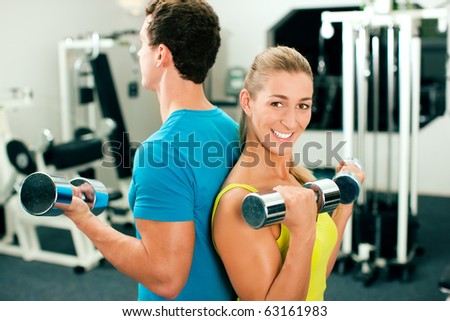 couple in the gym, rivaling each other, exercising with dumbbells (focus on the faces)